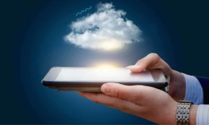Mãos segurando tablet, acima do aparelho há uma nuvem. Imagem remete à vitualização de dados.