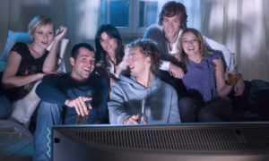 Jovens assistindo filme em casa e sorrindo. Imagem simboliza que estão assistindo a documentários de tecnologia.