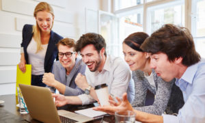 Equipe feliz de 5 pessoas olhando para o computador. Imagem simboliza equipes inovadoras seguindo o modelo de squads.