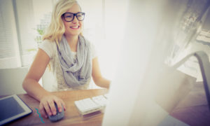 Mulher feliz em frente ao computador. Imagem simboliza o aumento de mulheres no mercado de TI.