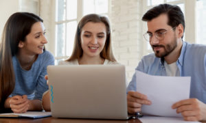 Três profissionais conversando em frente ao notebook. Imagem simboliza que ambos seguem a profissão Desenvolvedor Python.