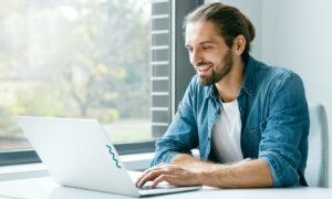 Homem sorrindo em frente ao computador. Imagem simboliza que ele é um Cientista de Dados.