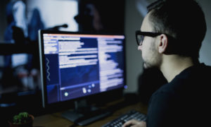 Profissional olhando para a tela do computador (homem). Imagem simboliza que ele é um Analista de Redes.