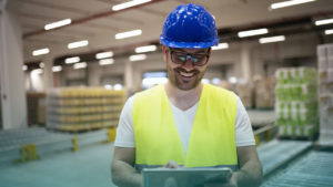 Profissional segurando tablet e sorrindo dentro de fábrica. Imagem simboliza que ele trabalha com tecnologias na Indústria 4.0.
