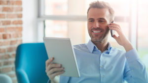 Homem segurando tablet e falando no celular sorrindo. Imagem simboliza que ele está simplificando o gerenciamento de dados com boas práticas.