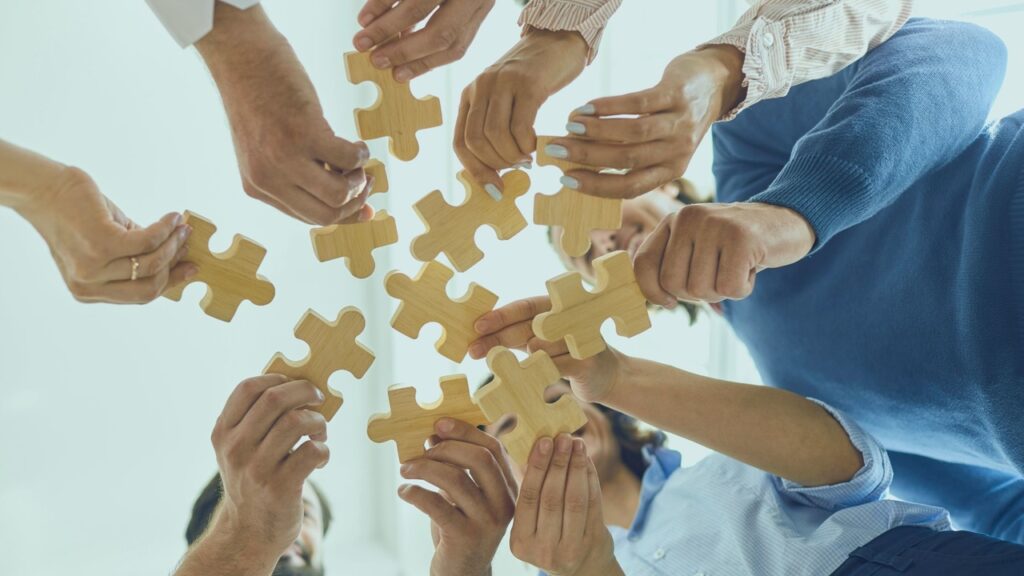 Pessoas unindo quebra-cabeça. Imagem simboliza que o fit cultural e a gestão de times impactam nos serviços de TI.