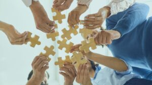 Pessoas unindo quebra-cabeça. Imagem simboliza que o fit cultural e a gestão de times impactam nos serviços de TI.